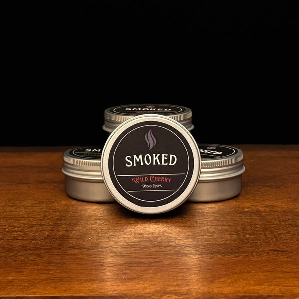 Four tins labeled 'Smoked' on a wooden surface with a black background. The front tin is Wild Cherry Flavored.