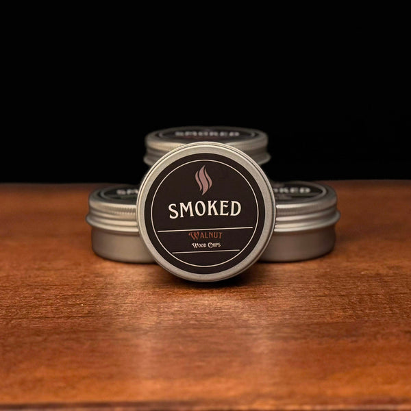 Four tins labeled 'Smoked' on a wooden surface with a black background. The front tin is Walnut Flavored.