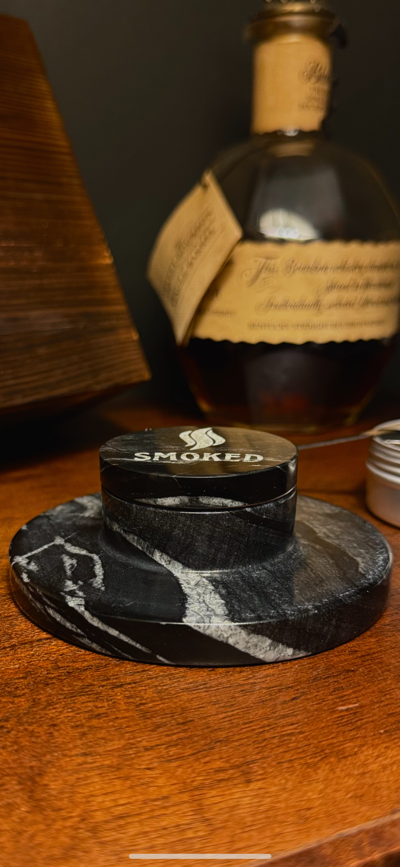 Black marble coaster with 'Smoked' label on a wooden surface, bottle in the background