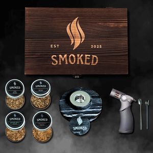 Marble cocktail smoker set with wooden box, smoking materials, and torch on a dark background.